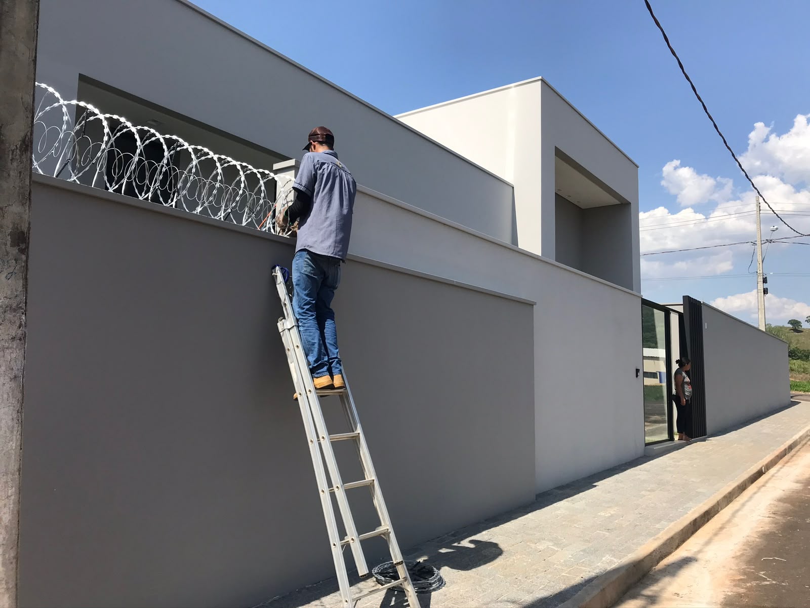 Técnico em escada instalando proteção em muro com concertina